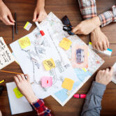 Picture of businessmen's hands on wooden table with documents, coffee and drafts