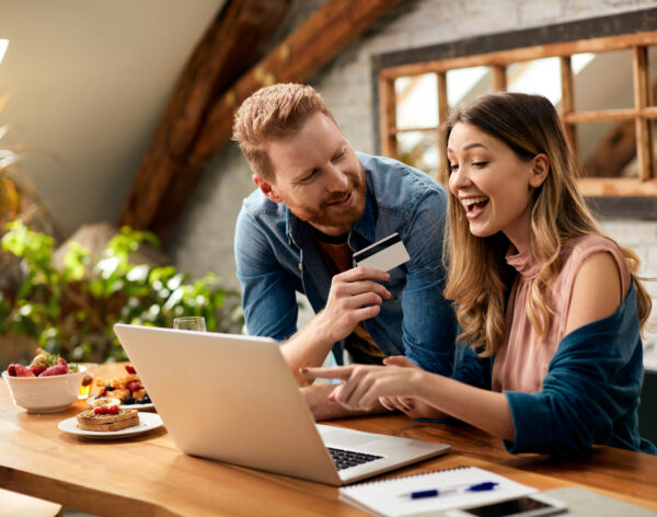 Happy woman pointing on something on laptop screen while shopping on the internet with her husband at home.