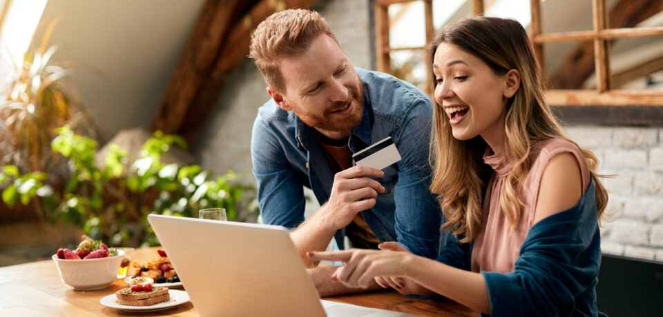 Happy woman pointing on something on laptop screen while shopping on the internet with her husband at home.